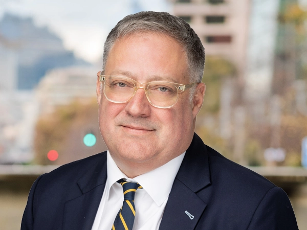 Portrait of Graeme Baxter, Director, Abu Dhabi, Standing outside featuring an urban cityscape with tall buildings and a mix of architectural styles. The scene includes some trees with autumn foliage, adding a touch of color. 