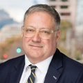 Portrait of Graeme Baxter, Director, Abu Dhabi, Standing outside featuring an urban cityscape with tall buildings and a mix of architectural styles. The scene includes some trees with autumn foliage, adding a touch of color.