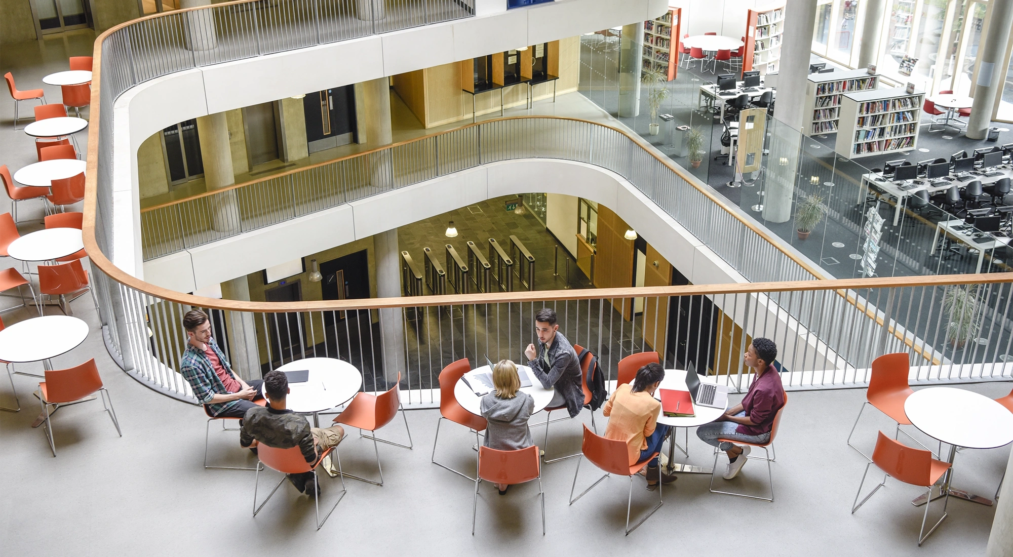 Furniture in open plan building with modern staircase and college students meeting friends.