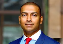 Portrait of Ajay Mangara, Project Director, outside in front of a blurred brown background featuring a building and mix of natural and urban elements.