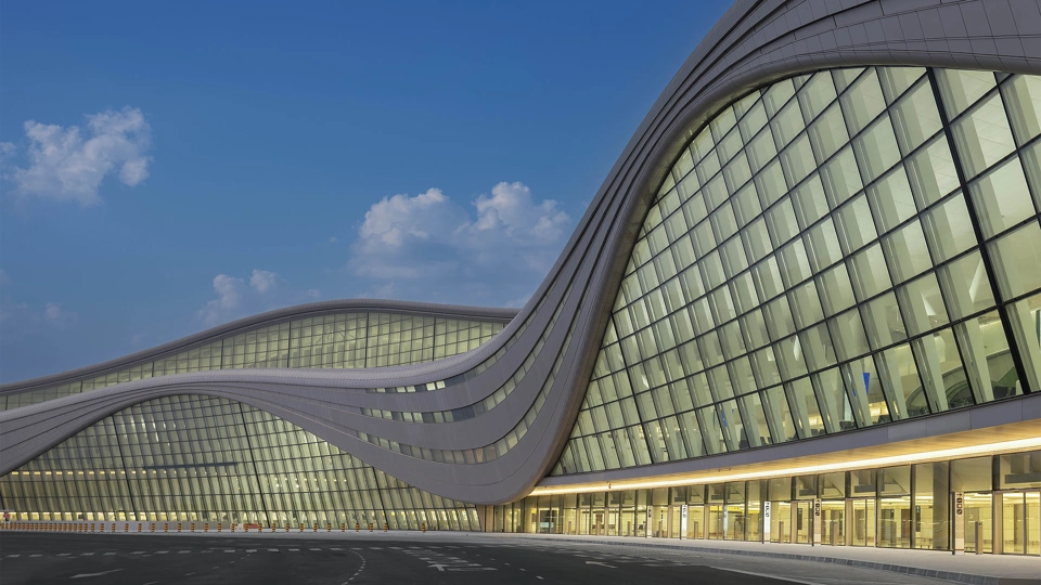 Modern, curved glass building with yellow lights aglow inside