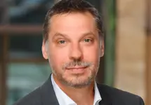 Kirk Smith, Director, Cost and Commercial Management, Germany and Austria,  outside in front of a blurred brown background featuring a building and mix of natural and urban elements.
