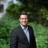 Sean Halpin, standing outside next to green bushes, smiling.