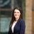 Anna Rosa, Clean energy sector lead, outside in front of a blurred brown background featuring a building and mix of natural and urban elements.