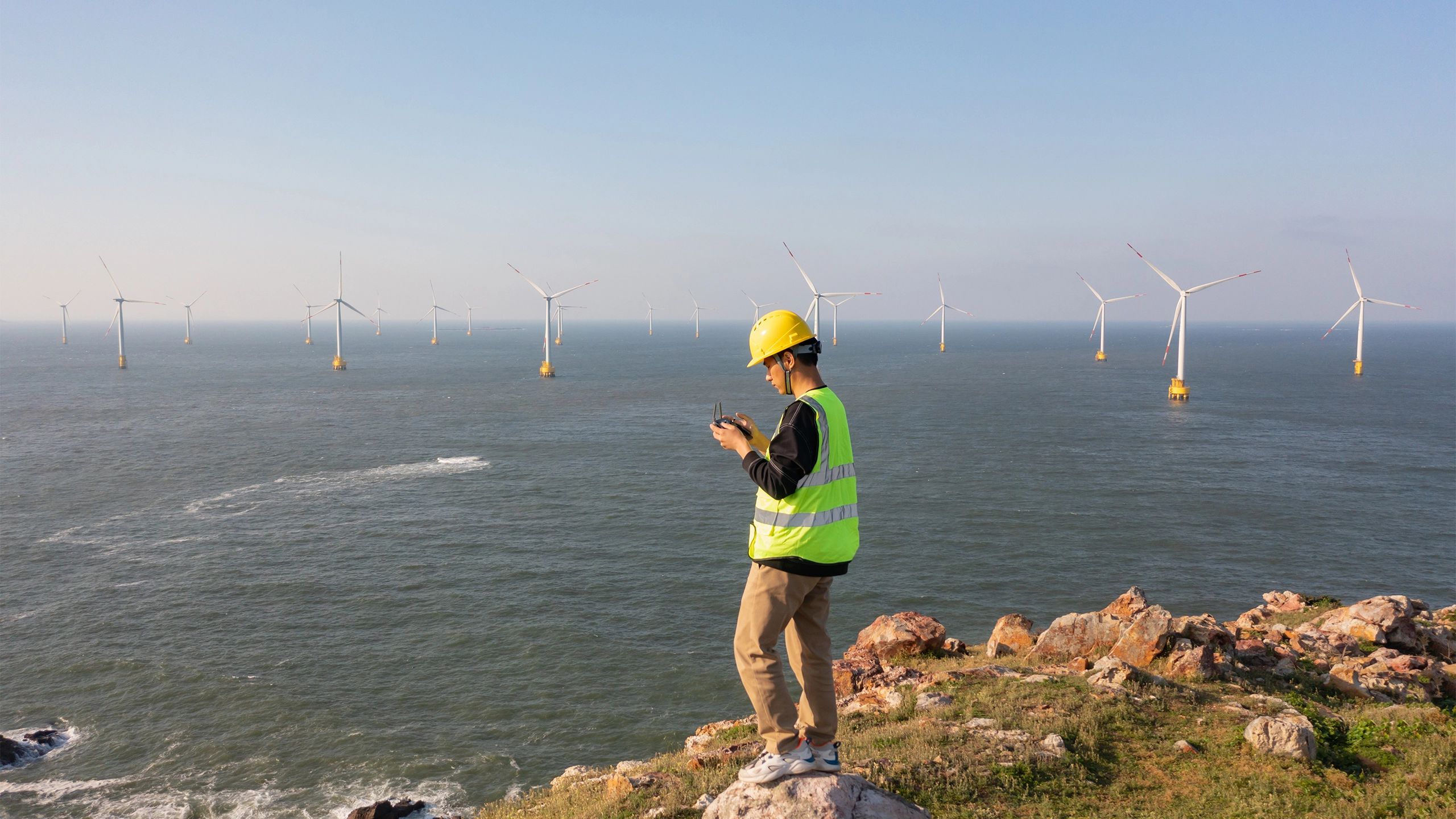Engineer in high-vis vest in front of an ocean of offshore wind turbines 