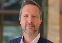 Portrait of Ben Jones, Senior Director, Head of Project Management, Advisory and Enterprise, Hong Kong, outside in front of a blurred brown background featuring a building and mix of natural and urban elements.