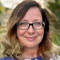 Portrait of Jessica Wergin, director, smiling in white shirt outside with green background.